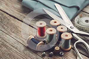 Retro sewing items - tailoring scissors, thimbles, buttons, wooden thread spools, measuring tape and green fabric