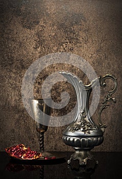 Retro still life with jug wine, metal goblet and a pomegranate