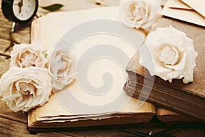 Retro still life with pale rose flowers and open ancient book. Nostalgic composition on old wooden table.