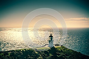 Retro style photo of Cape Reinga Lighthouse with sunshine over sea in the background. Summer evening at the northernmost