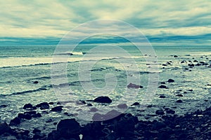 Retro-style photo of dark stormy day at Pacific ocean. Rip tide breaking at black rocks of the surf. Cape Egmont, New