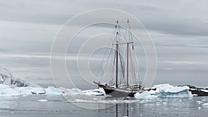 retro style sailing schooner during the huge iceberg in the Antarctic peninsula at the South Pole, waves of the southern