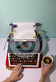 Retro style typewriter in dark gray and light gray with white sheet of paper. Bright flowers of different colors on the letters