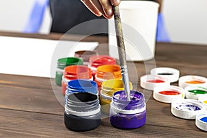 retro style wooden background. It has paint in cans and a brush for painting. A child in a white T-shirt dips a brush in the paint