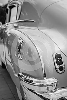 Retro-styled back of a classic car with headlights in black and white image. The headlights are finished in shiny chrome