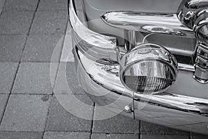 Retro-styled front of a classic car with round headlights in black and white image. The headlights are finished in shiny
