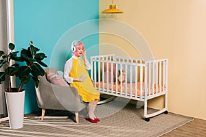 retro styled pregnant woman with pink hair listening music with smartphone