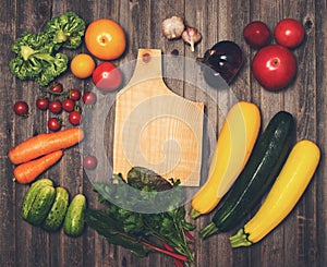 Retro styled vintage food background. Fresh vegetables and ingredients for cooking around cutting board on rustic weathered wood