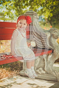 Retro stylish dressed blond young baby girl child posing in central park garden wearing french couturer white dress red bandana an