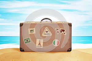 Retro suitcase with travel stickers on beach sand. Sea and blue sky in background