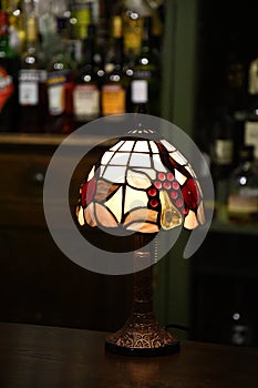 Retro table lamp with stained glass lampshade closeup on blurry background of bar. Glowing mosaic lamp in shape of dome. Vintage