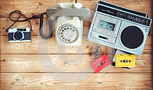 Retro technology of radio cassette recorder with retro tape cassette, vintage telephone and film camera on wood table.