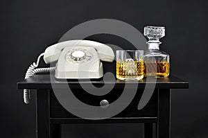 A retro telephone, a bottle and a glass with liquor on a table,