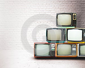 Retro televisions pile on floor in old room with white wall.