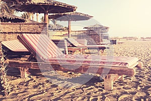 Retro toned image of a tropical beach with wooden sunbeds and umbrellas, summer vacation concept
