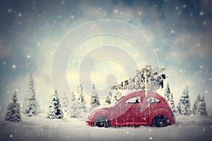 Retro toy car carrying tiny Christmas tree. Fairytale scenery with snow and forest.