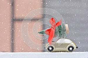 Retro toy car carrying tiny Christmas tree In Snowy Landscape. Christmas cards. Trucking.Delivery service.Copy space for text
