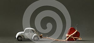 Retro toy car towing wooden red heart on a rope for valentine`s day at the blurred grey background