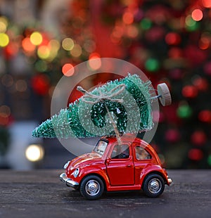 Retro toy red car carrying tiny Christmas tree on the background of christmas bokeh. Christmas cards. Trucking.Delivery service