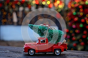 Retro toy red car, truck carrying tiny Christmas tree on the background of christmas bokeh. Christmas cards. Trucking.Delivery