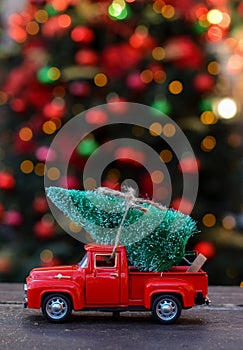 Retro toy red car, truck carrying tiny Christmas tree on the background of christmas bokeh. Christmas cards. Trucking.Delivery