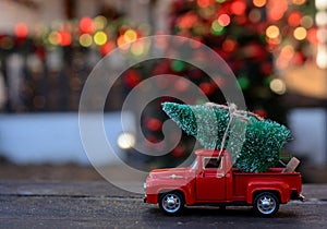 Retro toy red car, truck carrying tiny Christmas tree on the background of christmas bokeh. Christmas cards. Trucking.Delivery