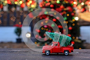 Retro toy red car, truck carrying tiny Christmas tree on the background of christmas bokeh. Christmas cards. Trucking.Delivery