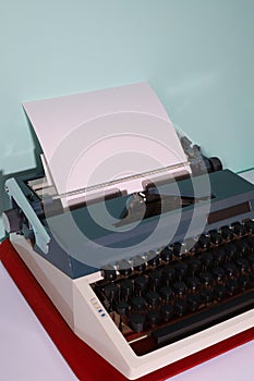retro typewriter in dark gray and light gray with a white sheet of paper. on a blue background