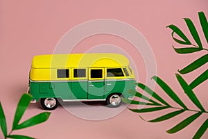 retro van among palm tropical leaves on a pastel pink background