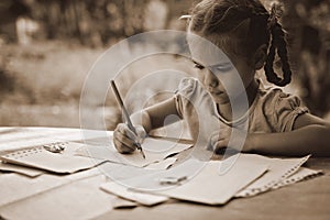 Retro and vintage concept. A little girl writing a letter with ink pen, old envelopes