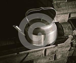 A retro & vintage metal kettle on a brick stove.