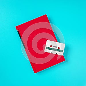 Retro white plastic audio cassette and red book laying on the green metal table.