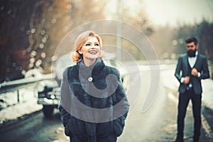 Retro woman in coat on road. Couple in love on romantic date. Bearded man and sexy woman in fur coat. Escort of girl by