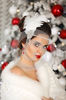 Retro woman Cristmas portrait. Brunette in white fur coat.  Elegant lady with feather in wedding hairstyle, beauty makeup and ruby