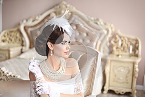 Retro woman portrait. Elegant brunette lady in hat with hairstyle, pearls jewelry set. Pretty female posing on modern armchair in