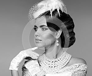 Retro woman portrait. Elegant lady with hairstyle, pearls jewelry set wears in hat and lace gloves posing isolated on studio gray