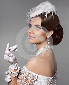 Retro woman portrait. Elegant lady with hairstyle, pearls jewelry set wears in hat and lace gloves posing isolated on studio gray