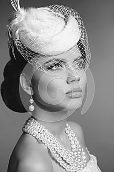 Retro woman portrait. Elegant lady with hairstyle, pearls jewelry set wears in hat with lace posing isolated on studio gray