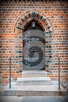 Retro wooden door with ornate iron knocker, handle and hinges in arched entrance with colorful bricks