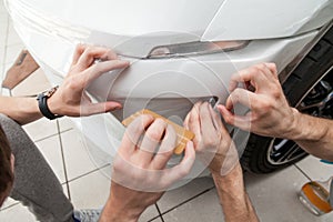 Retrofitting the car with a solid transparent protective film, the master smooths the surface by squeezing air bubbles with a