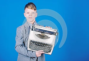 Retrospective study. Boy hold retro typewriter on blue background. What to do with this thing. Out of date. I need photo