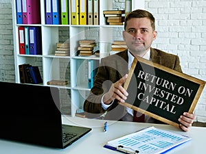 Return on invested capital ROIC. The accountant holds a sign.