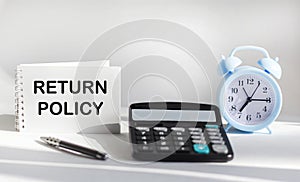 RETURN POLICY text written on notepad, next to calculator, clock and pen on white background