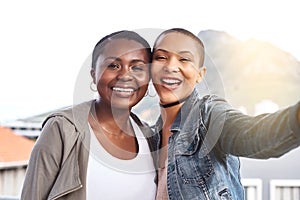 Reunited at last. Portrait of two young women smiling and posing while taking a selfie in the city.