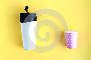 Reusable black and white takeaway coffee cup with disposable paper cup isolated on yellow background