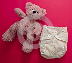 Reusable cloth baby diaper. Eco friendly nappy and teddy bear on red background