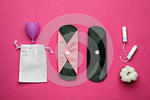 Reusable cloth pads and menstrual cup near disposable tampons on pink background, flat lay