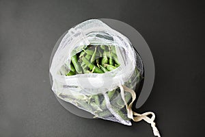 Reusable eco-friendly bag full of fresh seasonal pea pods on black background