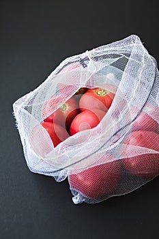 Reusable eco-friendly bag full of fresh seasonal tomatoes on black background