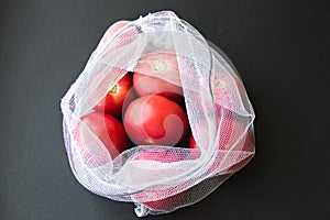 Reusable eco-friendly bag full of fresh seasonal tomatoes on black background